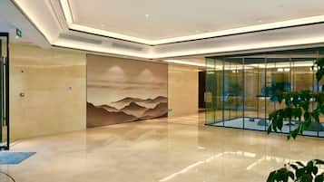 A modern lobby with a large wall mural, a glass partition, and a polished floor.