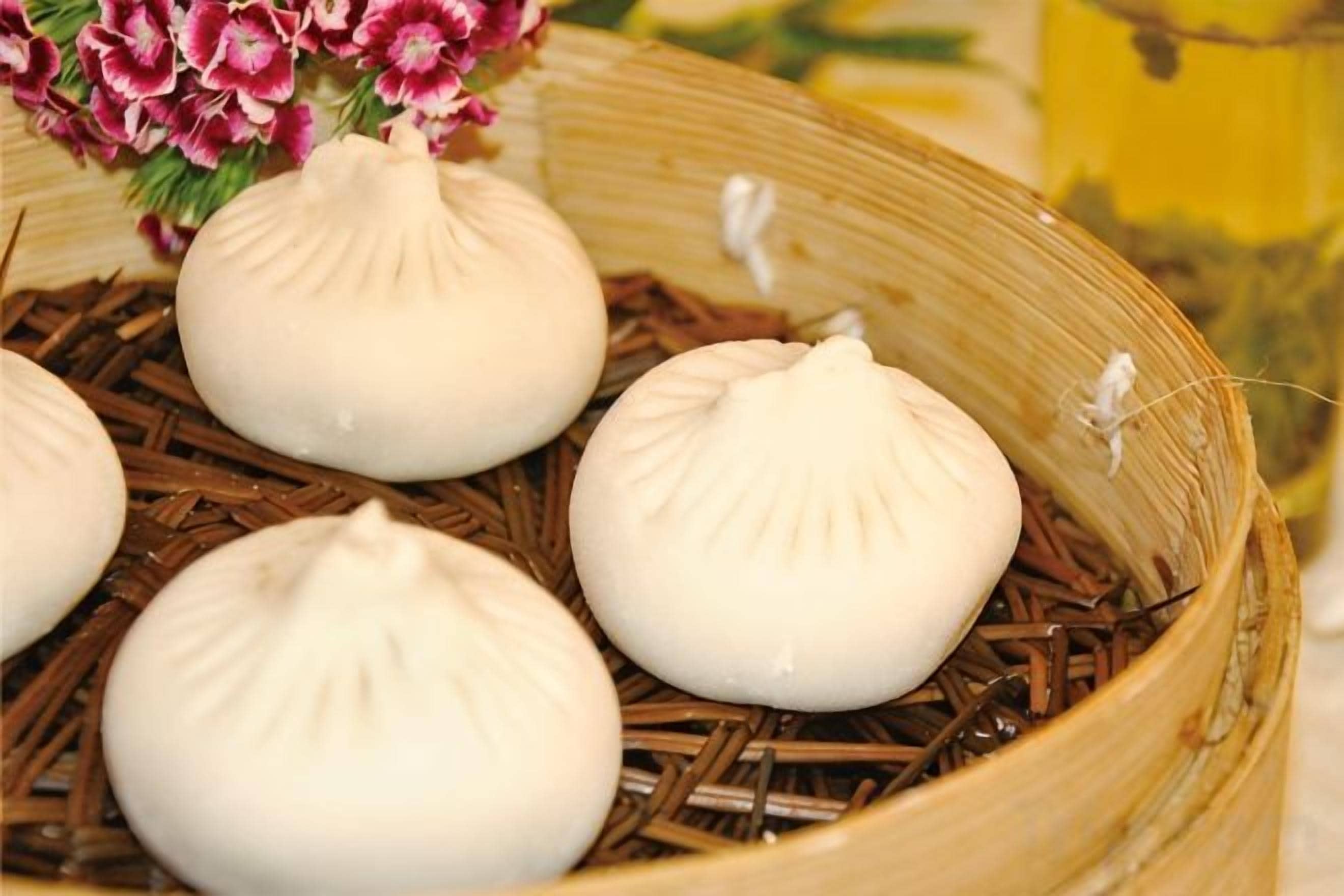 Una vaporera de bambú con varios dumplings blancos sobre una base de paja.