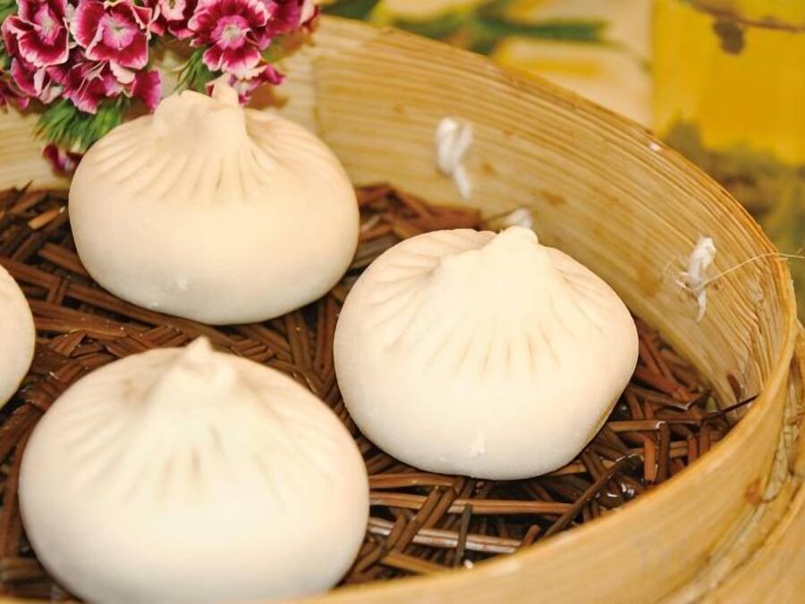 Una vaporera de bambú con varios dumplings blancos sobre una base de paja.