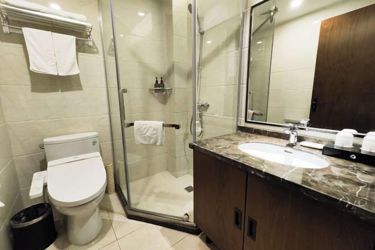 Un baño con inodoro, ducha con mampara de vidrio, lavabo y un espejo grande.