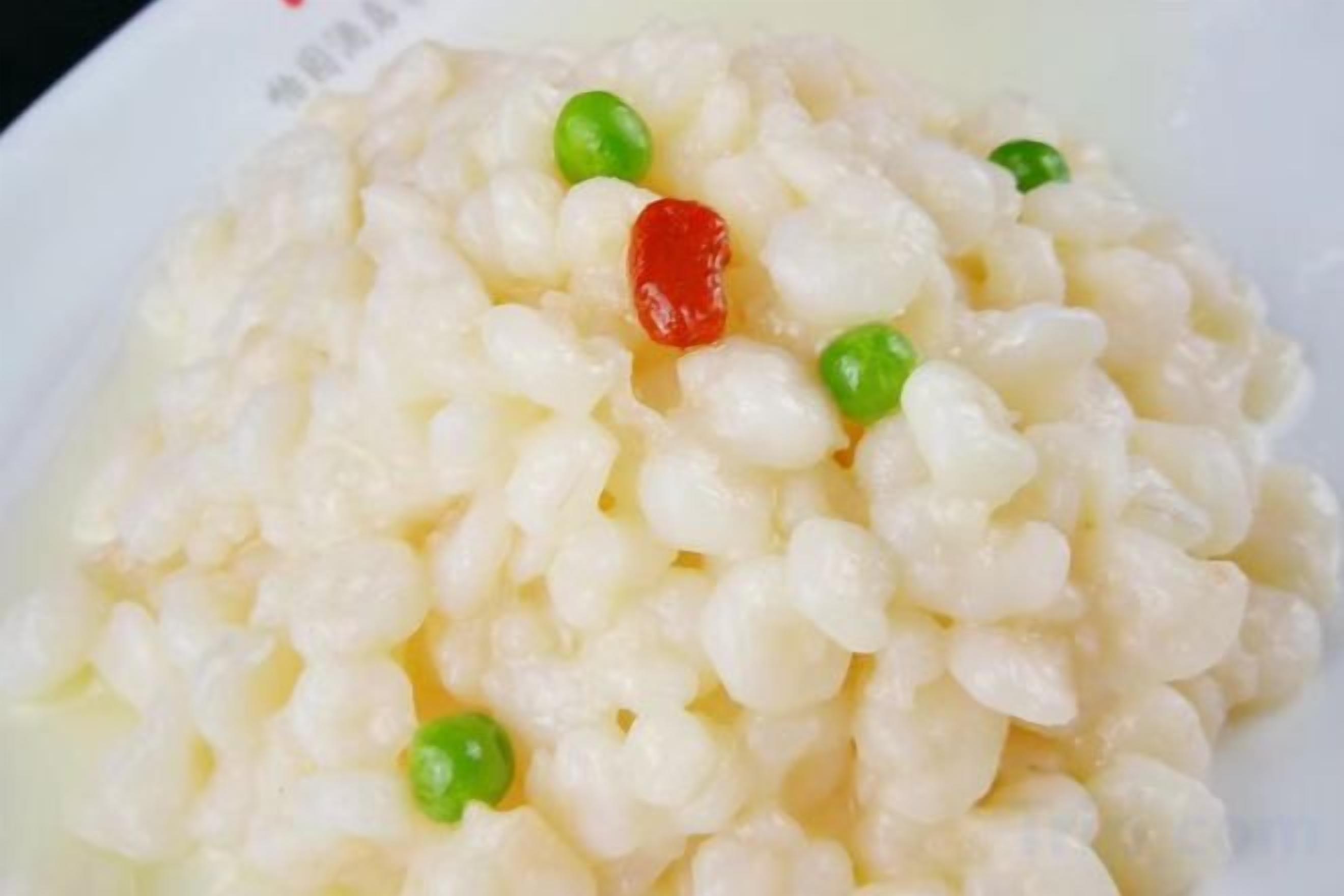 A close-up of a dish with rice, peas, and a red item, possibly a fruit or garnish.