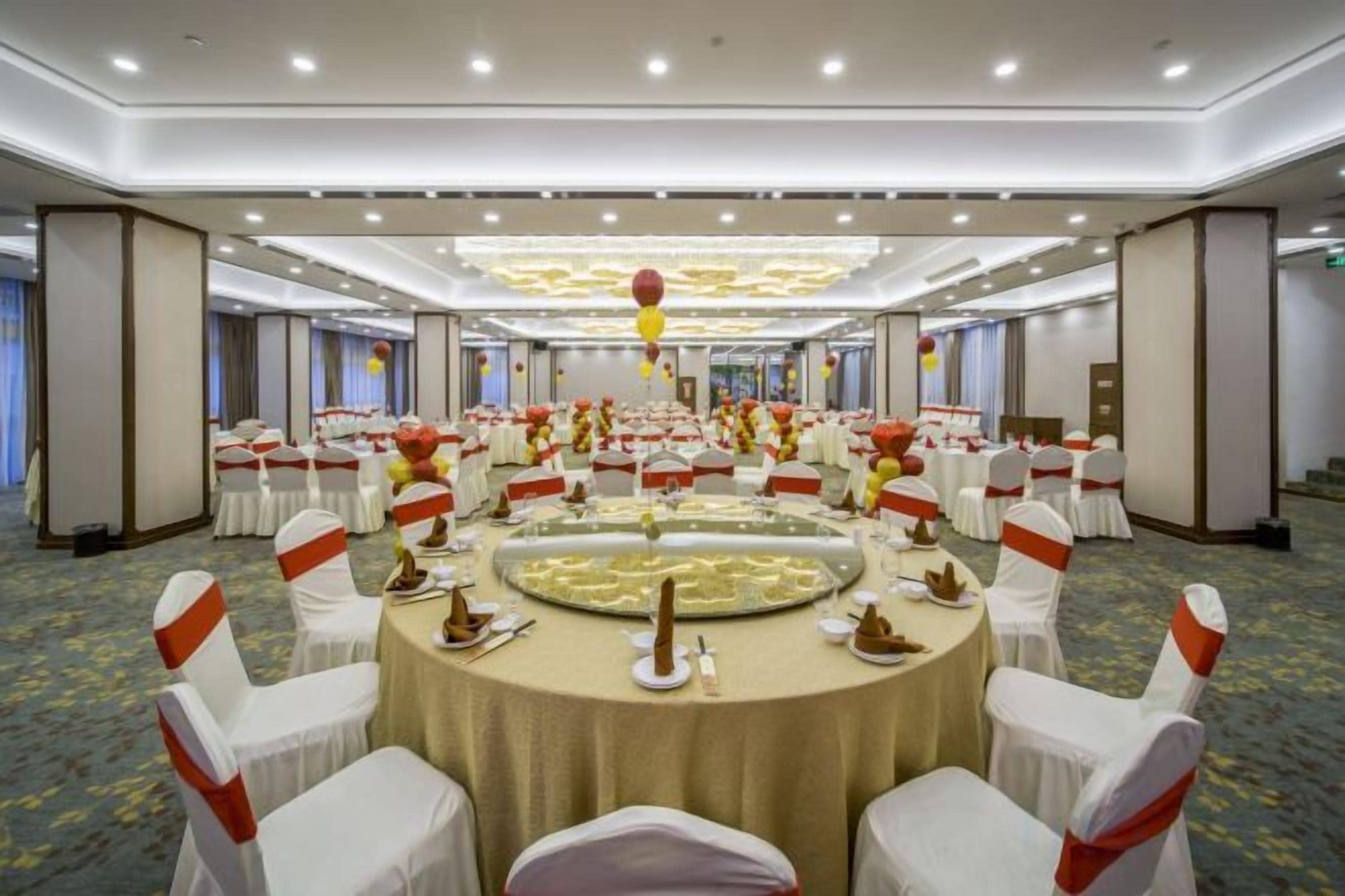 Une salle de banquet avec des tables rondes, des chaises blanches et des rubans rouges.