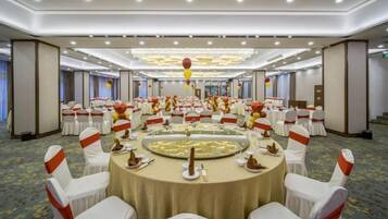 A banquet hall with round tables, white chairs, and red sashes.