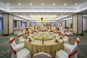 Un salón de banquetes con mesas redondas, sillas blancas y cintas rojas.