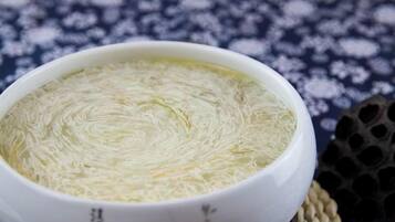 En skål med klar suppe og en let ru overflade, stillet på en vævet måtte.