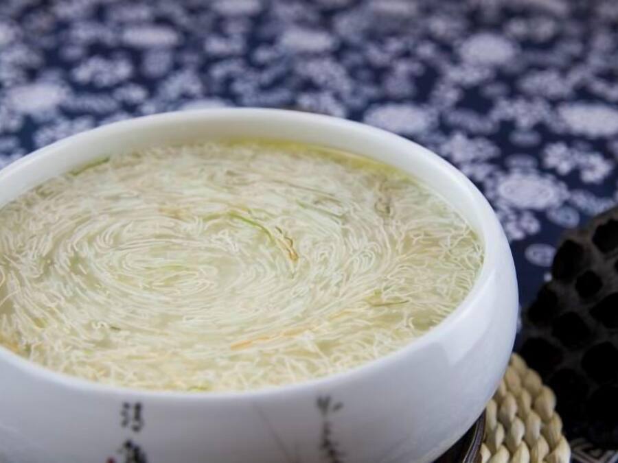 En skål med klar suppe og en let ru overflade, stillet på en vævet måtte.
