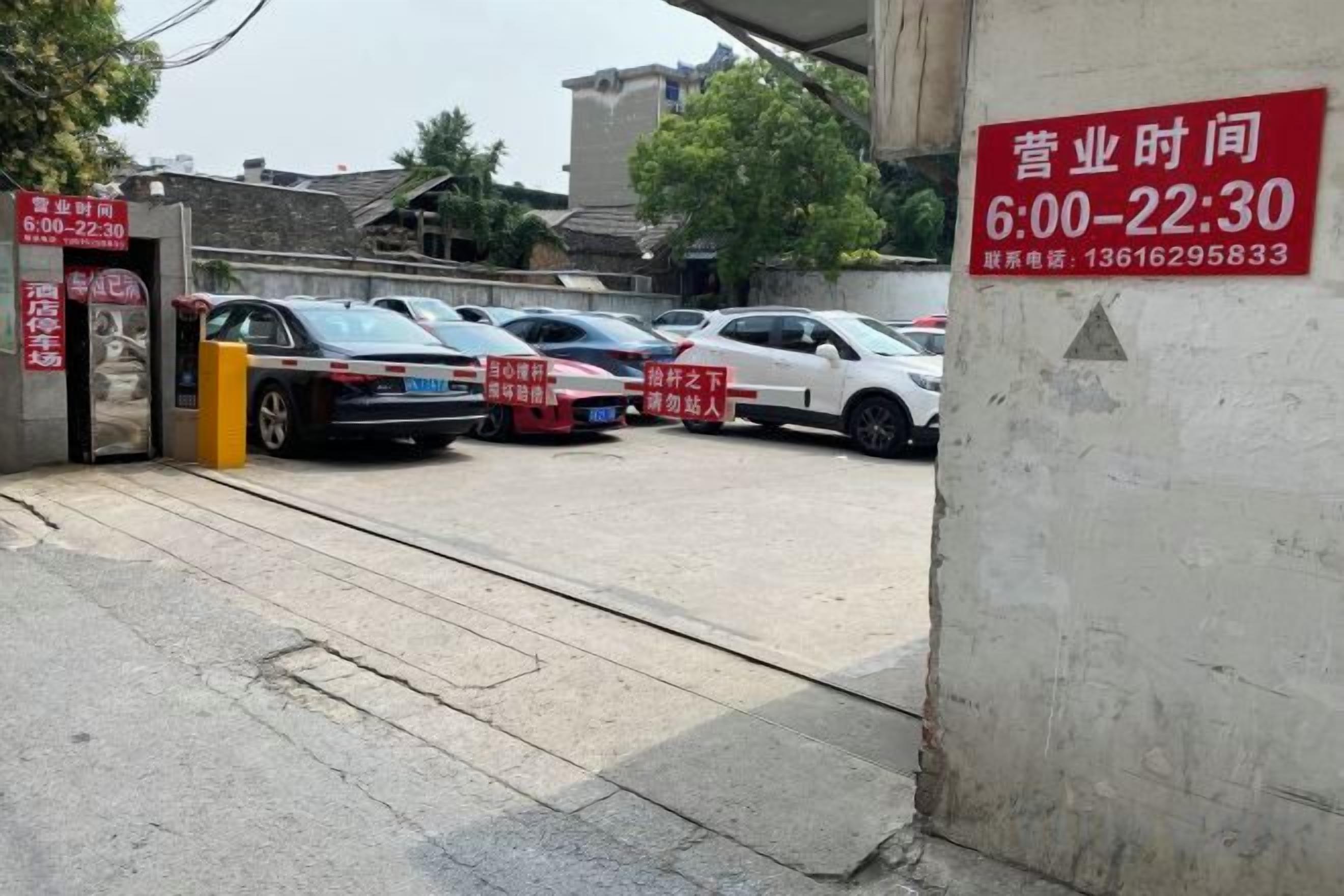 Un'area di parcheggio con auto e un cartello che indica gli orari di apertura.