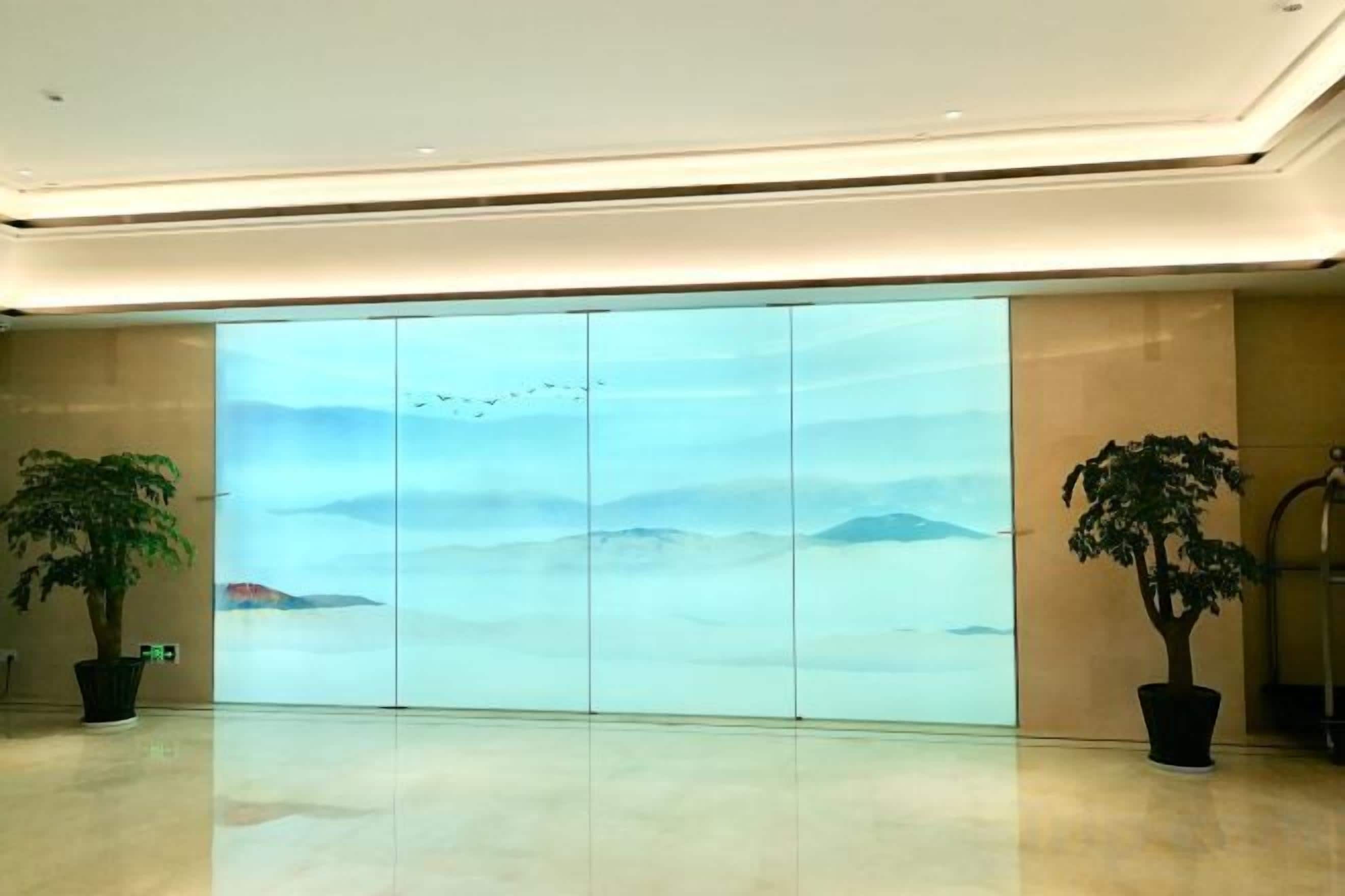 A spacious lobby with a large glass wall displaying a scenic view, two potted plants, and a clean, modern floor.