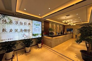A hotel reception area with a reception desk, potted plants, and a large digital display. - Yiyuan Hotel (Yangzhou)