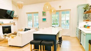 A spacious living area with a large white sofa, a kitchen island with stools, and a TV mounted on the wall.