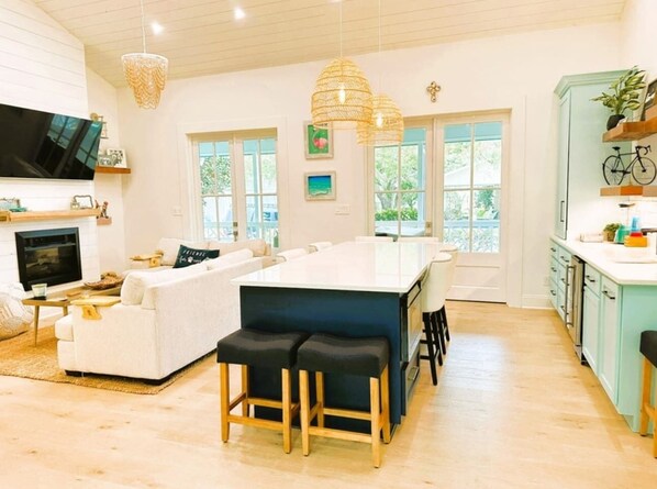 A spacious living area with a large white sofa, a kitchen island with stools, and a TV mounted on the wall.