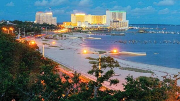A coastal cityscape with a beach, a marina, and several high-rise buildings.