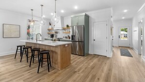 A modern kitchen with a central island, stainless steel appliances, and wooden bar stools. - Designer House-Pool-Walk 2 beach (Panama City Beach)