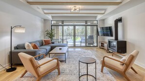 A modern living room with a grey sofa, two beige armchairs, a coffee table, and a TV. - 104 Verbier Building 11 (Mont-Tremblant)