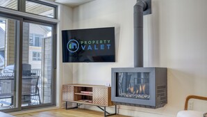 A modern living room with a fireplace, a television mounted on the wall, and a sliding glass door leading to an outdoor area. - 104 Verbier Building 11 (Mont-Tremblant)