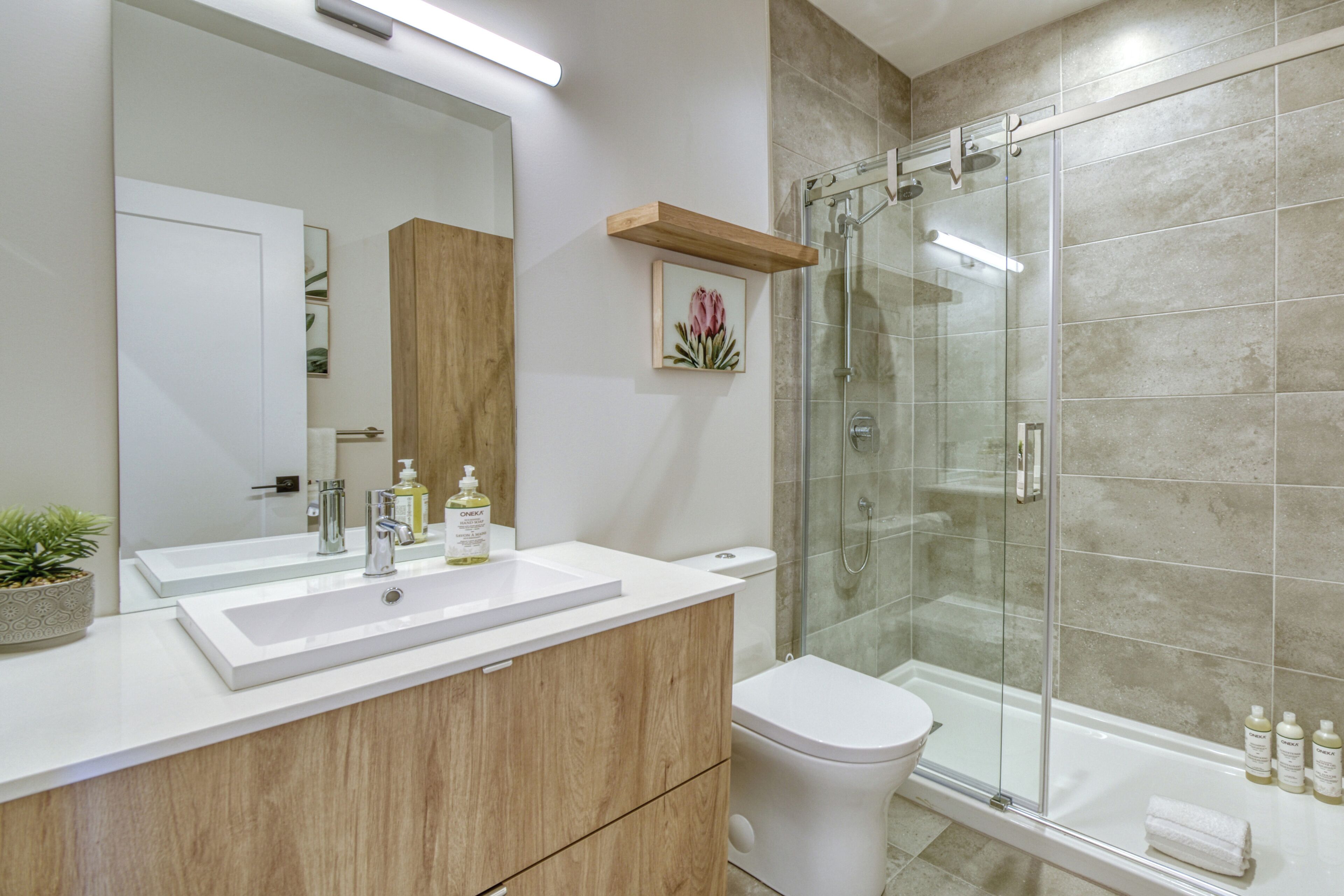 A modern bathroom with a white sink, wooden vanity, a glass shower enclosure, and a toilet.
