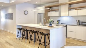 A modern kitchen with a central island, bar stools, a refrigerator, and a clock on the wall. - 104 Verbier Building 11 (Mont-Tremblant)