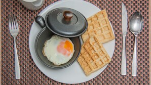 A plate with a fried egg, waffles, and a pot with a lid on a woven placemat.