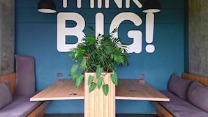 A modern seating area with a large wall mural that reads "THINK BIG!" and a central wooden table with a potted plant.