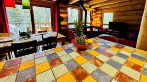 A wooden cabin interior with a dining table, chairs, a red sofa, and a fireplace.