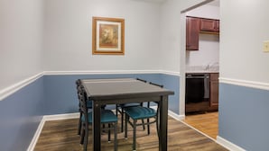 A dining area with a table and chairs, a painting on the wall, and a kitchen in the background. - HomeTowne Studios by Red Roof Huntsville - Madison (Madison)