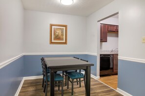 Un comedor con mesa y sillas, un cuadro en la pared y una cocina al fondo.