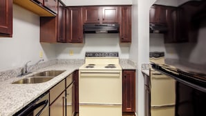 A kitchen with wooden cabinets, a white stove, and granite countertops. - HomeTowne Studios by Red Roof Huntsville - Madison (Madison)