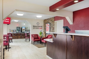 Un hall de hotel con mostrador de recepción, sillas rojas, un reloj y un letrero que indica acceso a Wi-Fi.