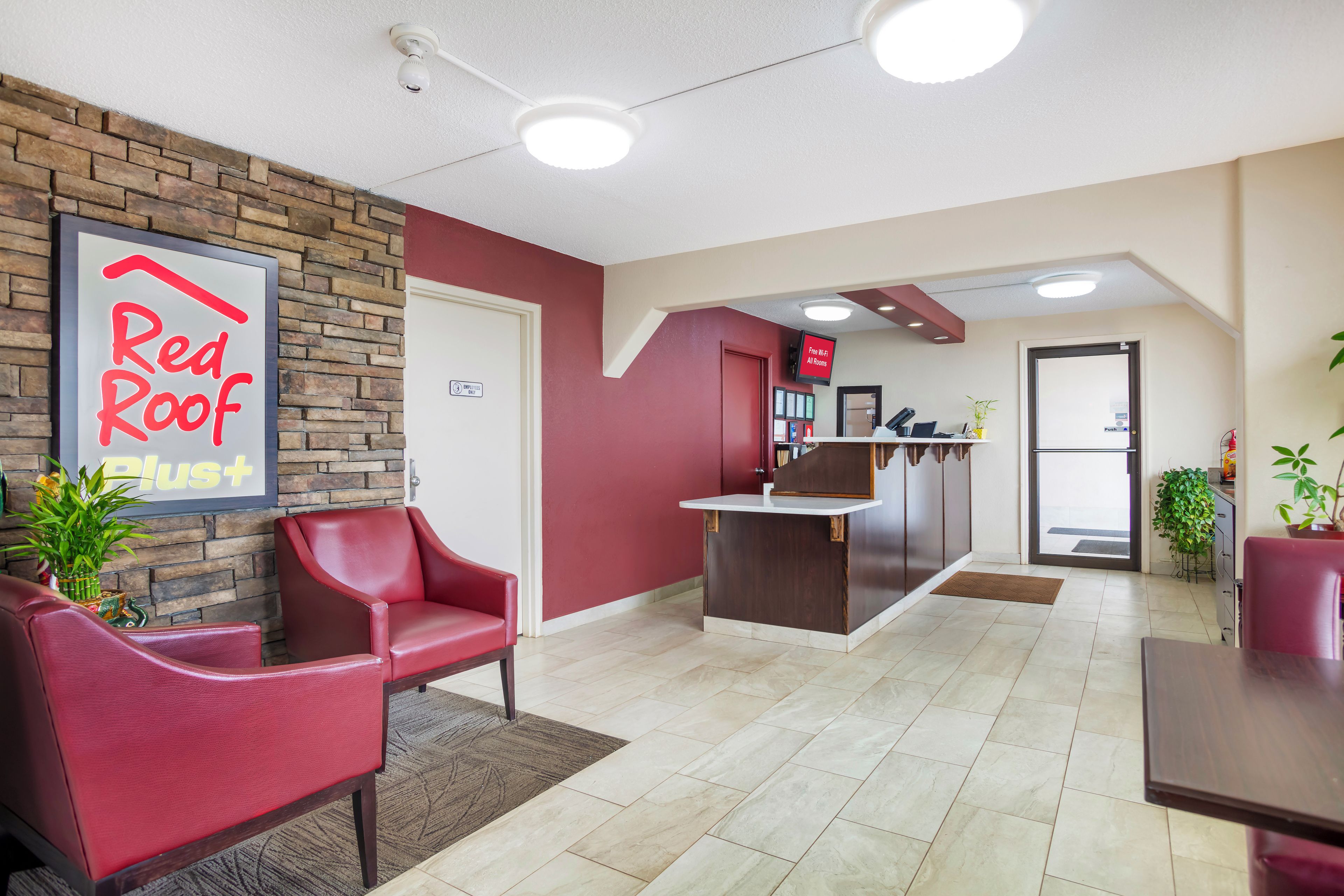 A reception area with a Red Roof Plus sign, a reception desk, and seating.