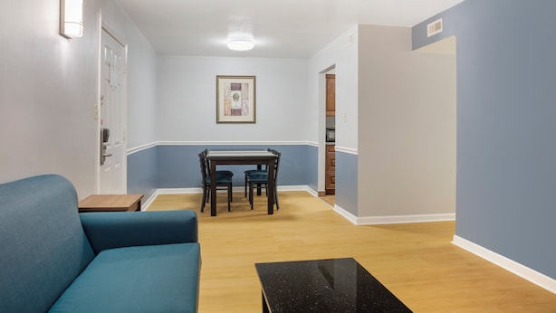A room with a blue sofa, a dining table with chairs, and a black coffee table. - HomeTowne Studios by Red Roof Huntsville - Madison (Madison)