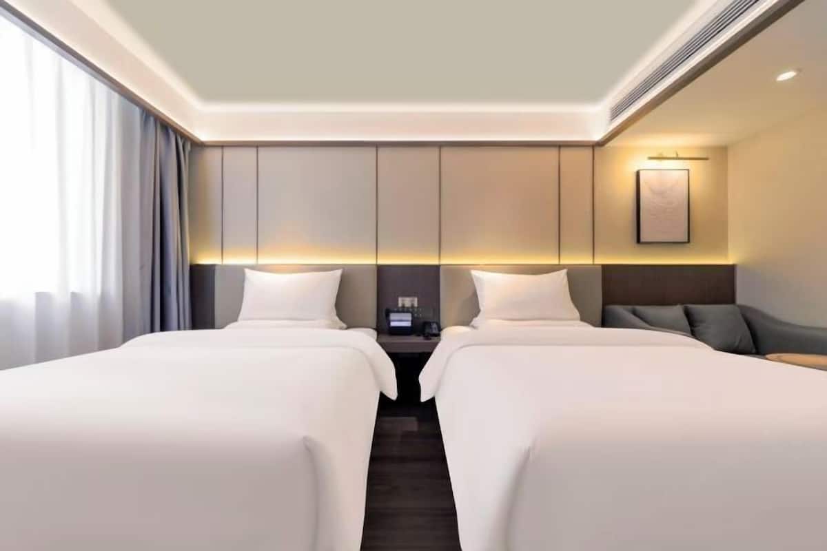 Een hotelkamer met twee bedden, een nachtkastje, een lamp en een lijst aan de muur.