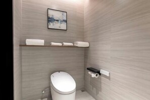 Une petite salle de bain comprenant des toilettes, une étagère avec des serviettes et un tableau encadré au mur.
