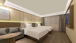 Ein modernes Hotelzimmer mit einer Couch, zwei Betten, einem kleinen Tisch und einem Bild an der Wand.