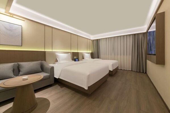 Une chambre d’hôtel moderne avec un canapé, deux lits, une petite table et un tableau au mur.