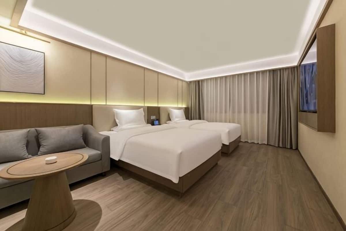 Een moderne hotelkamer met een bank, twee bedden, een kleine tafel en een groot raam met gordijnen.