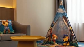 Ein gemütlicher Raum mit einer Couch, einem kleinen gelben Tisch und einem bunten Spielzelt mit Zeichentrickfiguren.