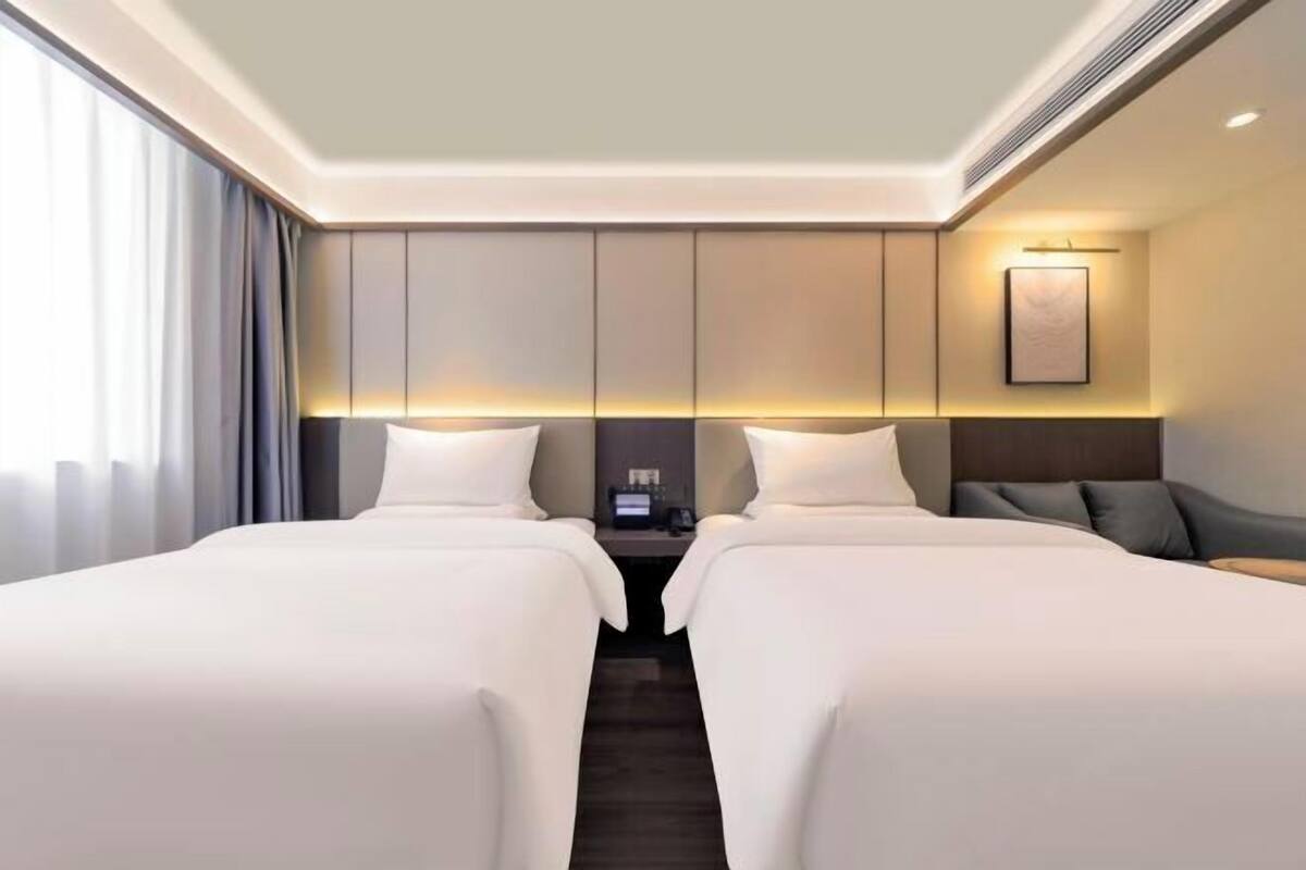 Een hotelkamer met twee bedden, een nachtkastje, een lamp en een ingelijste foto aan de muur.
