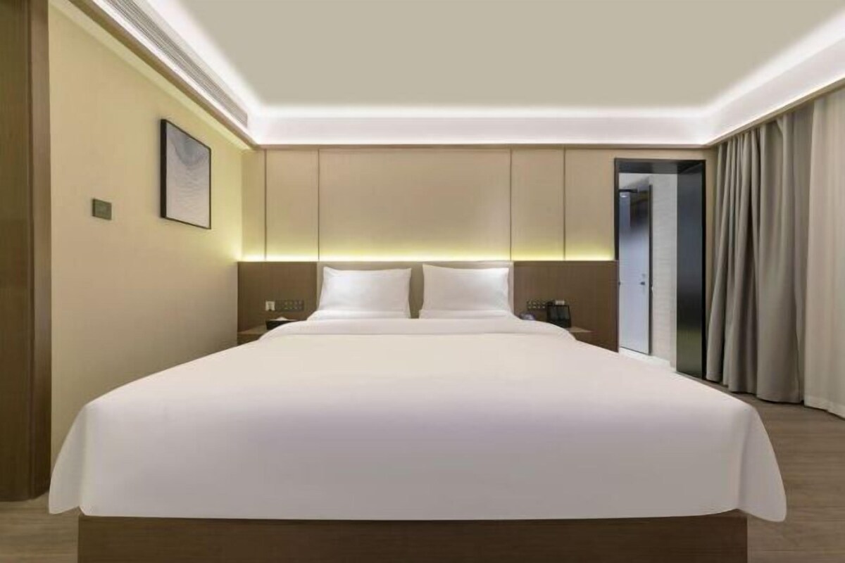 Une chambre d’hôtel avec un grand lit, une table de chevet, une commode, une lampe fixée au mur et une porte avec des rideaux.