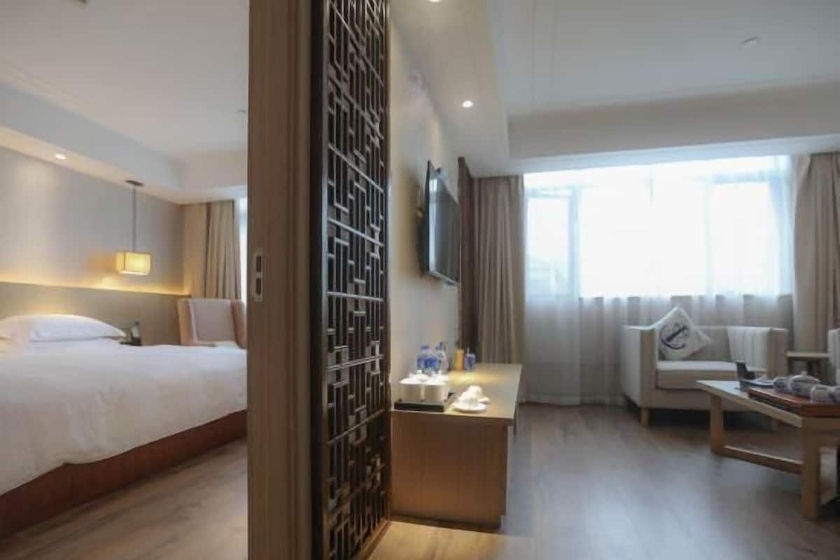 Quarto de hotel com cama, escrivaninha, cadeira, televisão e janela com cortinas.