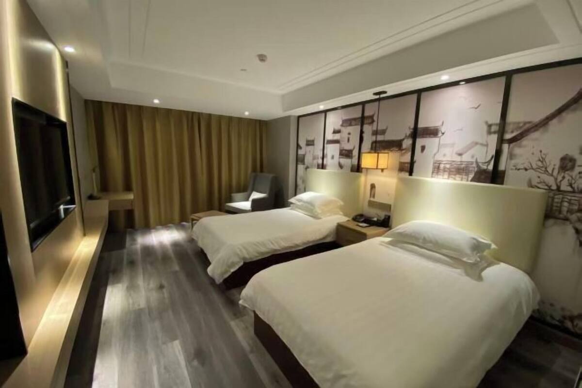 Quarto de hotel com duas camas, uma televisão de tela plana, uma cadeira e uma parede com arte decorativa tradicional.