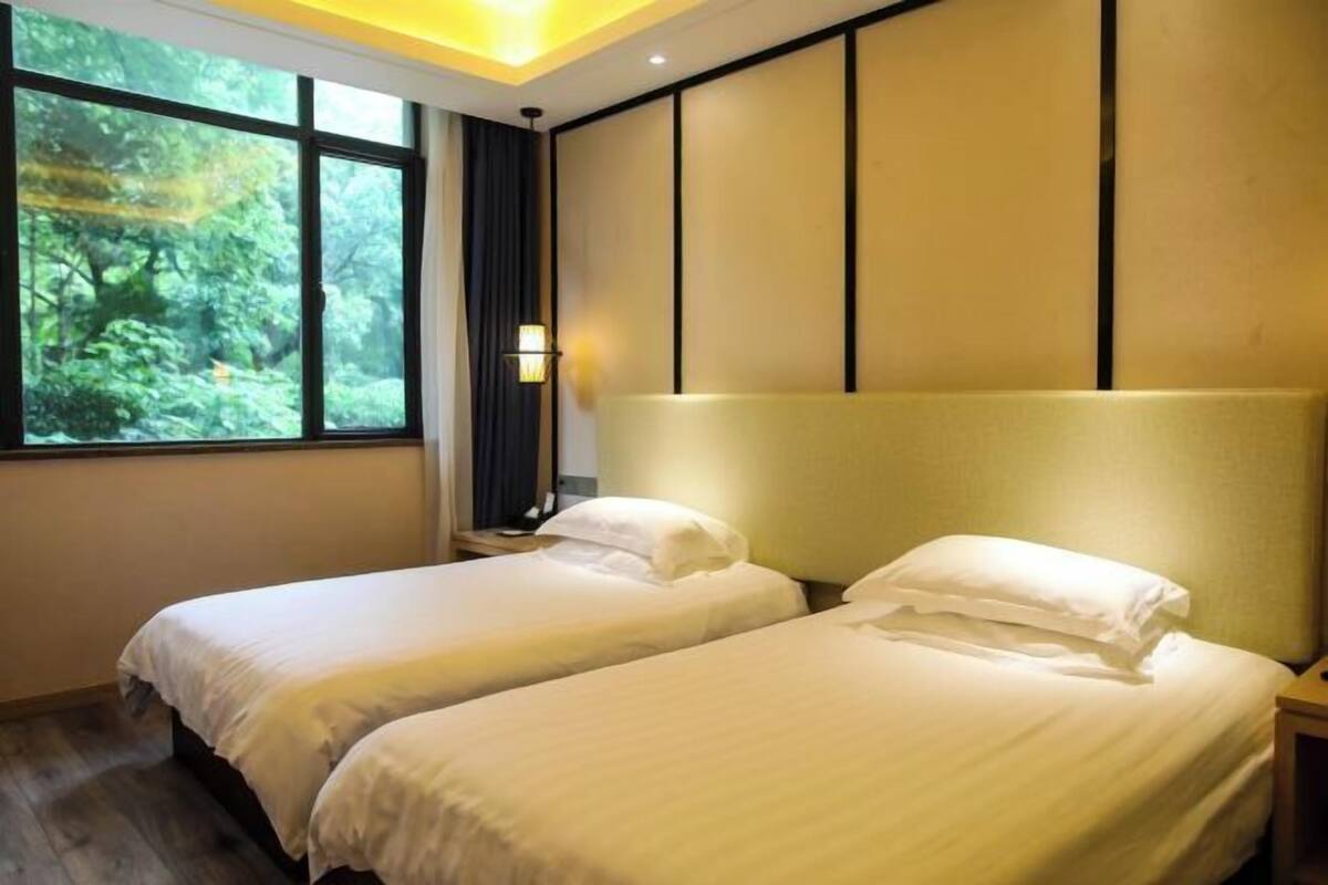 Quarto de hotel com duas camas, uma janela grande com vista para o verde e uma parede com lambris.