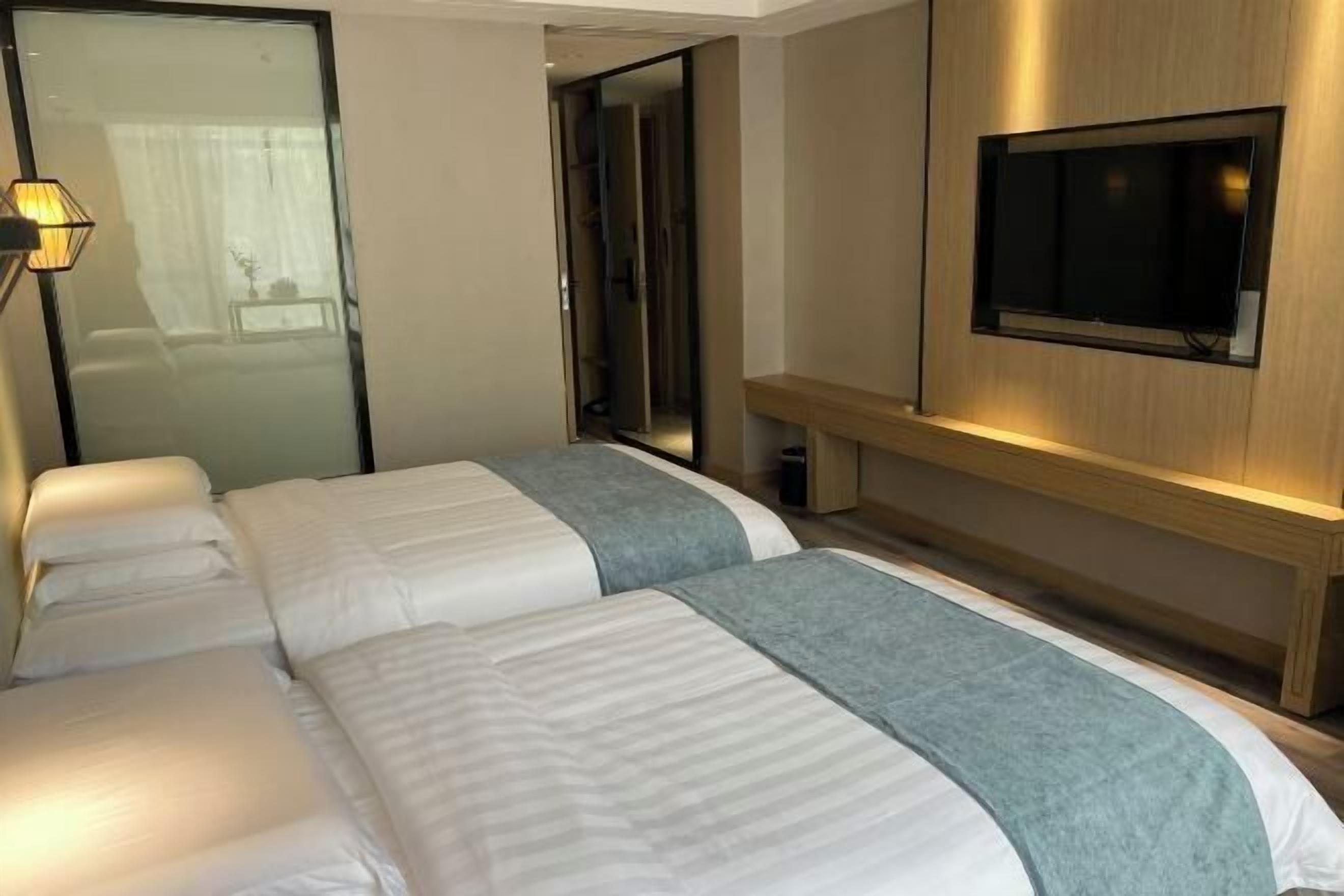 A hotel room with two beds, a TV mounted on the wall, and a mirror.