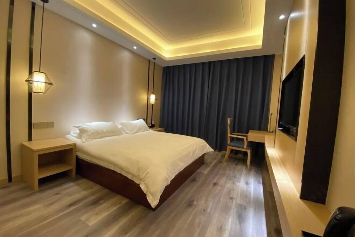 Quarto de hotel moderno com uma cama grande, mesas de cabeceira, escrivaninha e televisão fixada na parede.