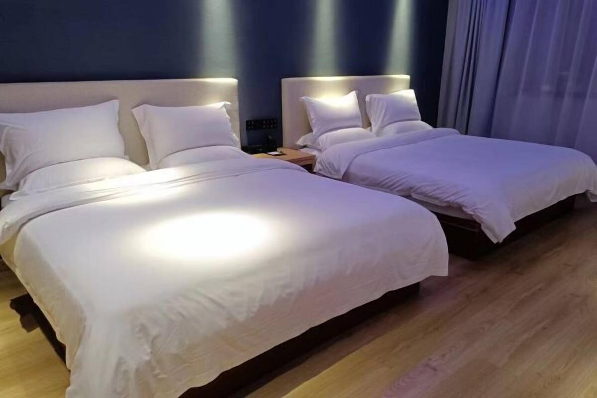 Quarto de hotel com duas camas, uma mesinha de cabeceira e piso de madeira.