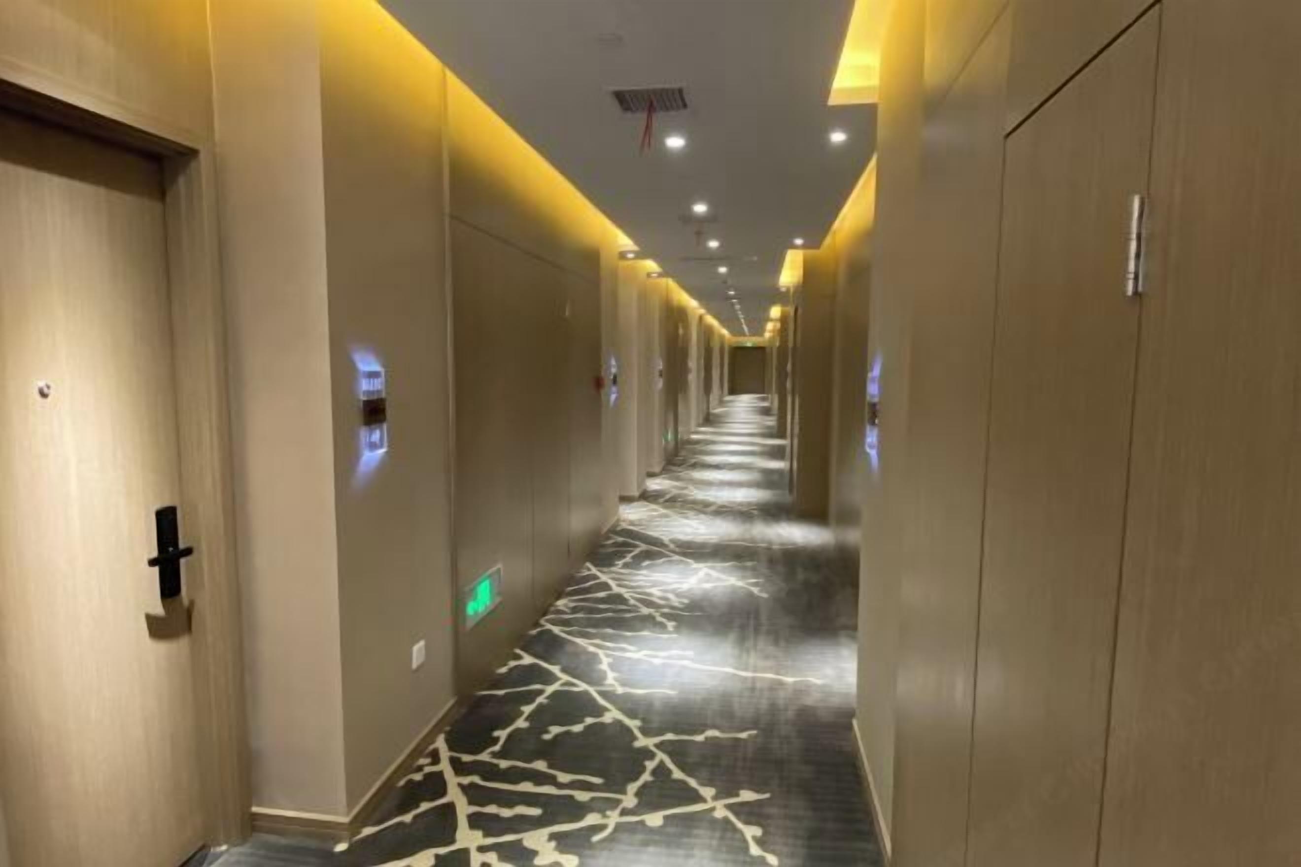 Un couloir d’hôtel avec un tapis à motifs, des portes en bois et un éclairage encastré.