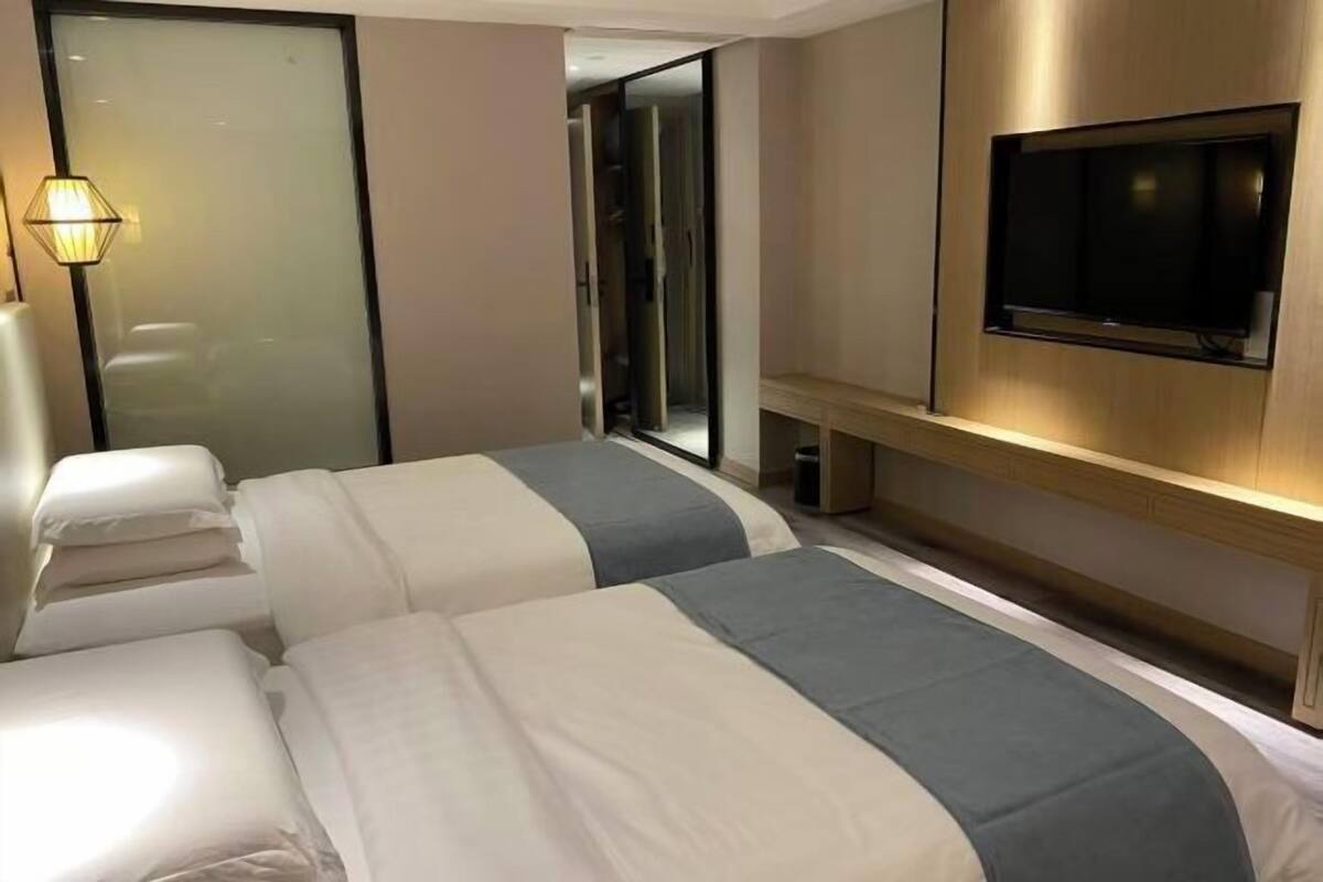 Quarto de hotel com duas camas, uma televisão, um espelho e um abajur.