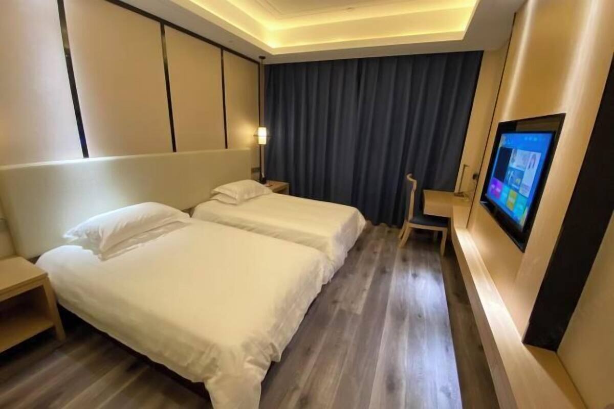 Quarto de hotel com duas camas, televisão de tela plana, escrivaninha e cortina escura.