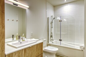 A modern bathroom with a large mirror, a sink, a toilet, and a glass-enclosed shower area. - 105 Verbier Building 12 (Mont-Tremblant)