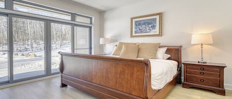 A bedroom with a large bed, a nightstand, a lamp, and a window with a view of trees.