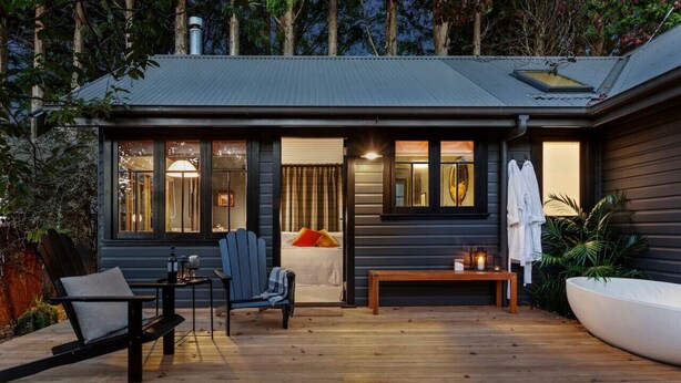 Une cabane moderne dotée d’une terrasse, d’un lit et d’un coin salon.